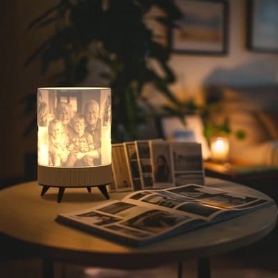Nebula personalizirana 3D foto lampa koja svijetli na okruglom stolu pokraj otvorenog obiteljskog foto albuma u ugodnoj dnevnoj sobi.